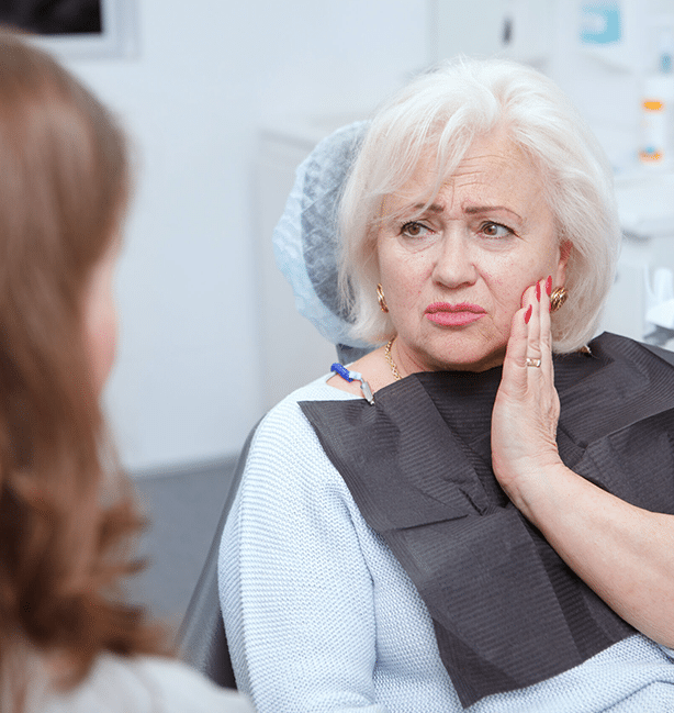 Older woman touching cheek in discomfort during dental examination at clinic