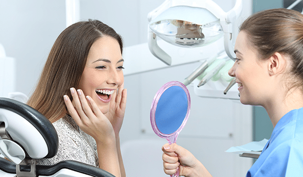 Dental patient examining smile in mirror with hygienist in modern dental office.